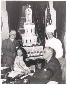 FDR pictured receiving a birthday cake decorated with checks for the National Foundation for Infantile Paralysis. January, 1942